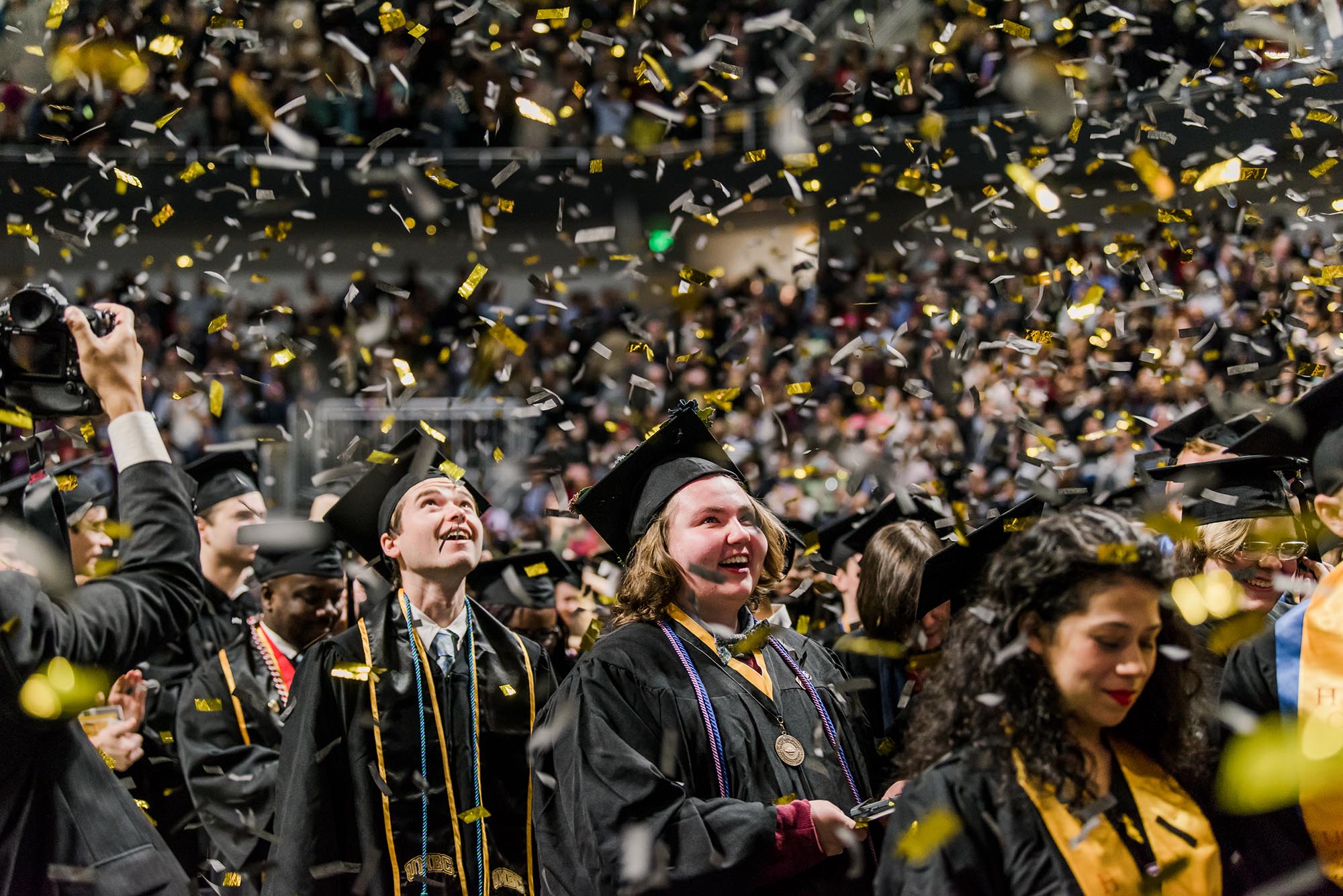Undergraduate students look up at a flurry of black and gold confetti.